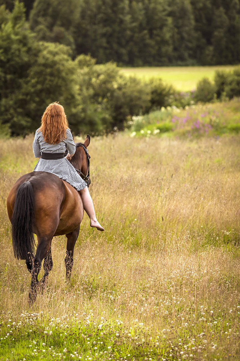 Kvinna rider ut på sommaräng med häst